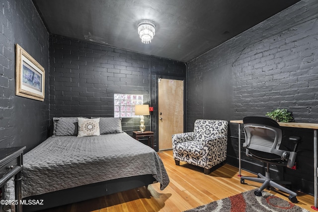 bedroom featuring brick wall and wood finished floors