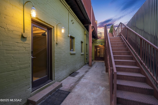 property exterior at dusk with a patio, brick siding, and stairway