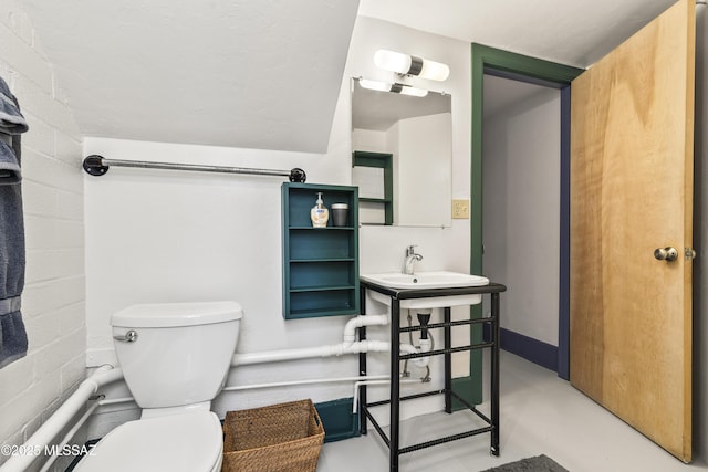 half bathroom featuring toilet, a sink, concrete flooring, and concrete block wall