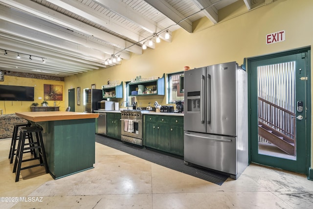 kitchen featuring green cabinets, a breakfast bar area, beamed ceiling, stainless steel appliances, and open shelves