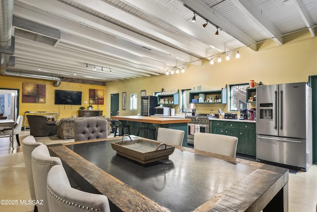 dining space with concrete flooring, beam ceiling, indoor wet bar, and rail lighting