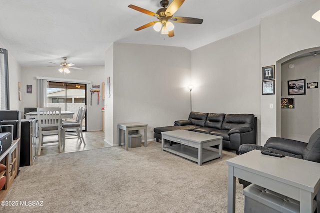 living room with a ceiling fan, arched walkways, light carpet, and vaulted ceiling