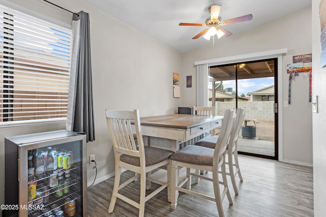 dining area with a ceiling fan, wine cooler, baseboards, and wood finished floors