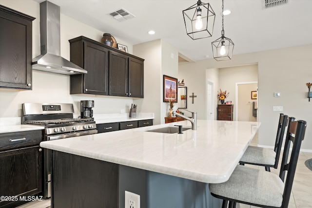 kitchen with gas stove, a center island with sink, visible vents, a sink, and wall chimney range hood