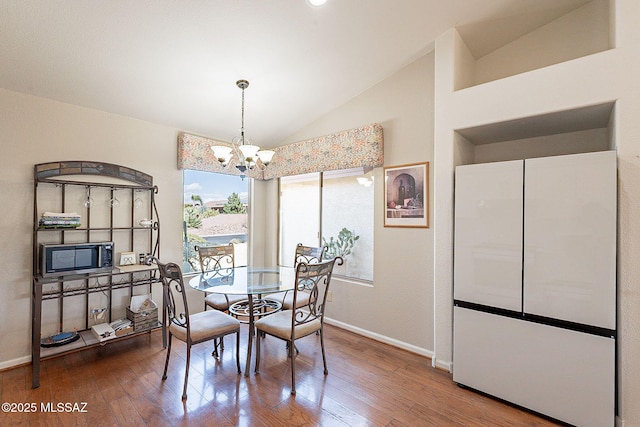 dining space with a notable chandelier, vaulted ceiling, baseboards, and hardwood / wood-style flooring