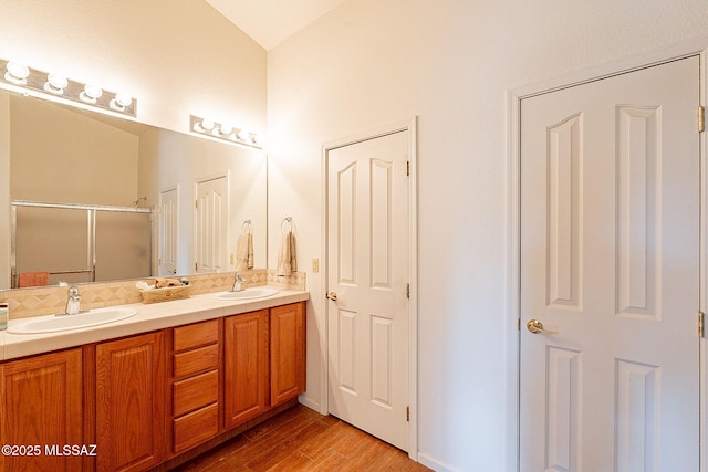 full bath featuring double vanity, a shower stall, a sink, and wood finished floors