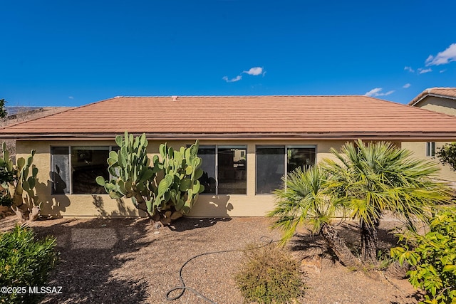 rear view of house with a tiled roof and stucco siding