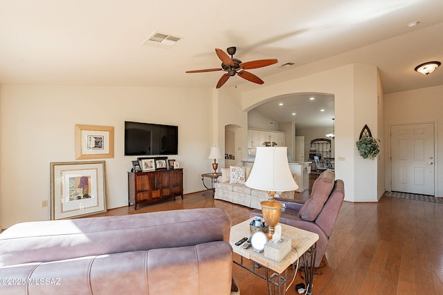 living room featuring lofted ceiling, visible vents, arched walkways, and hardwood / wood-style floors