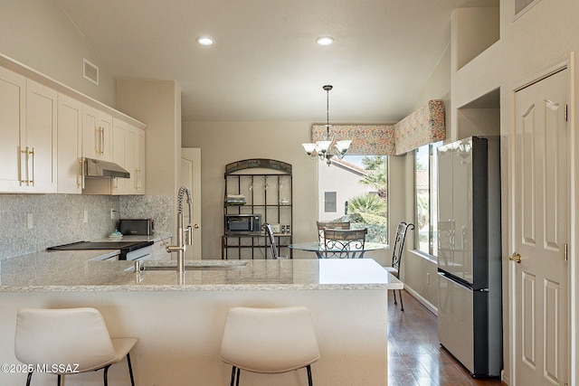 kitchen with under cabinet range hood, a peninsula, range with electric stovetop, backsplash, and freestanding refrigerator