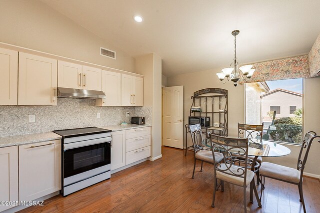 kitchen with under cabinet range hood, electric range, visible vents, vaulted ceiling, and tasteful backsplash