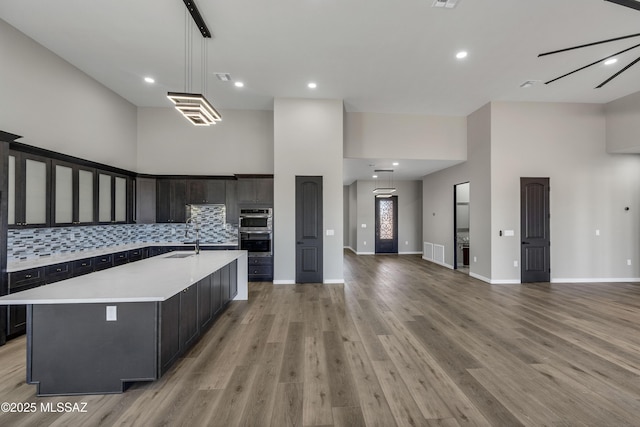 kitchen with a spacious island, stainless steel double oven, light wood-style floors, light countertops, and decorative backsplash