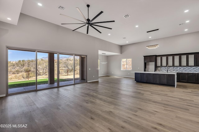 unfurnished living room featuring visible vents, baseboards, light wood-style floors, and a towering ceiling