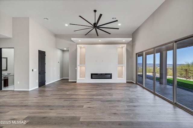 unfurnished living room with a glass covered fireplace, recessed lighting, wood finished floors, and visible vents