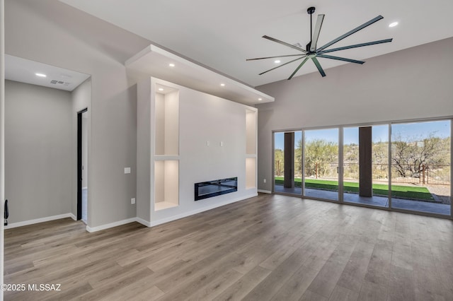 unfurnished living room featuring recessed lighting, baseboards, a glass covered fireplace, and wood finished floors