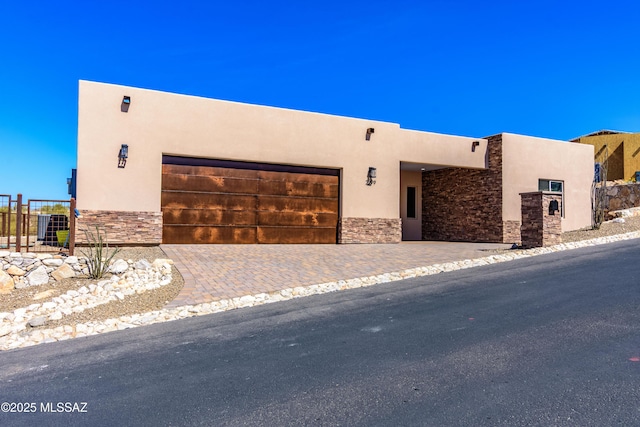 pueblo-style house with a garage, fence, stone siding, and stucco siding