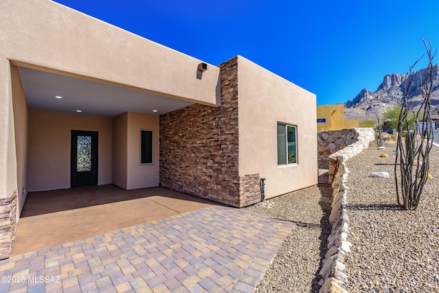 view of property exterior featuring stucco siding, stone siding, a patio, fence, and a mountain view