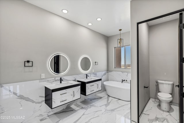 bathroom with a freestanding tub, two vanities, marble finish floor, a sink, and recessed lighting