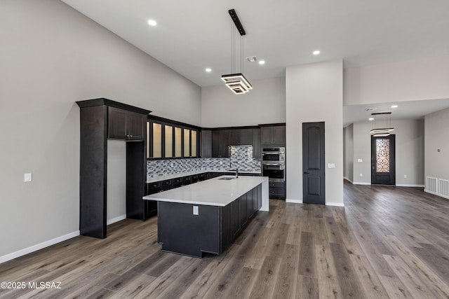 kitchen featuring wood finished floors, a sink, light countertops, a towering ceiling, and backsplash