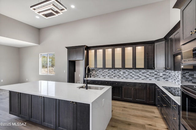 kitchen featuring backsplash, light countertops, an island with sink, light wood-style flooring, and a sink