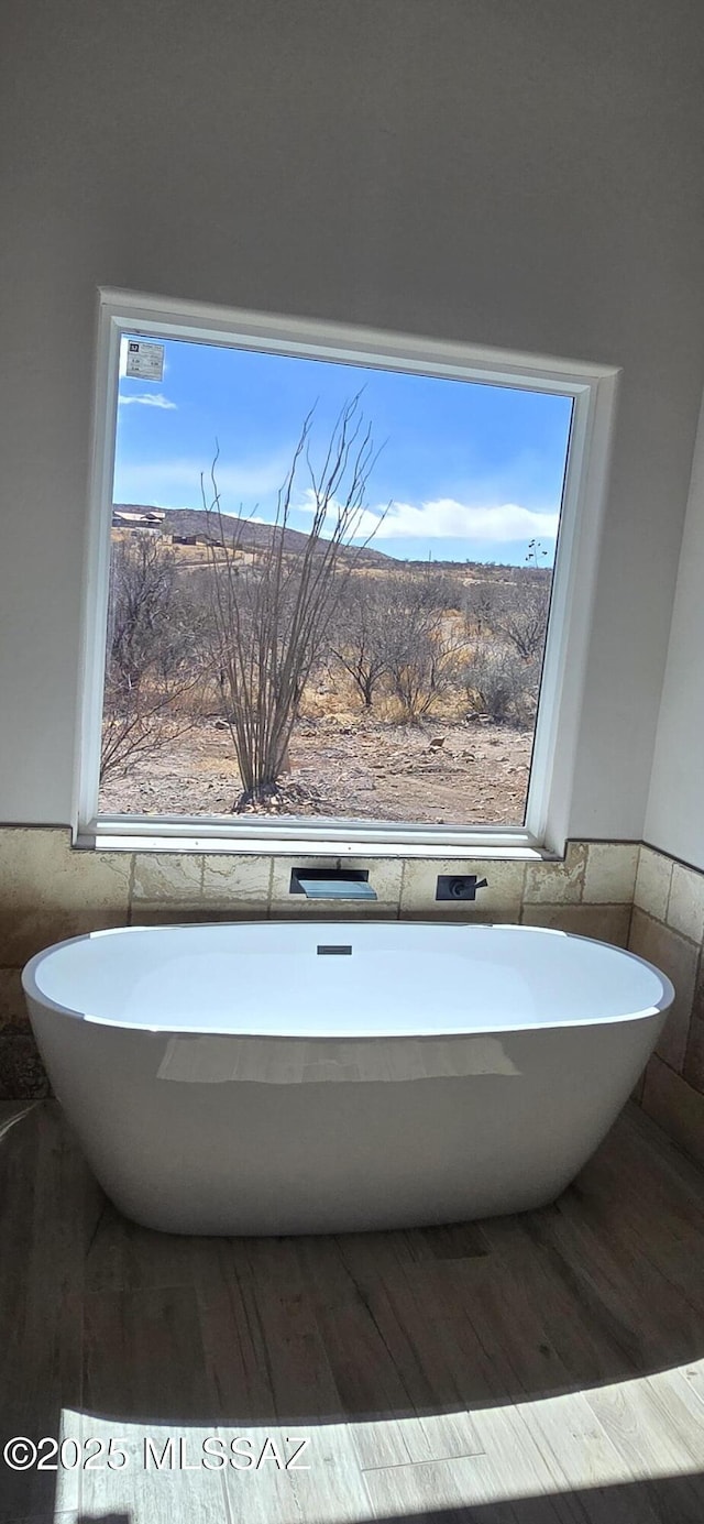 full bathroom featuring a wainscoted wall, tile walls, a freestanding tub, and wood finished floors