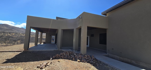 exterior space with a patio area, a mountain view, and stucco siding