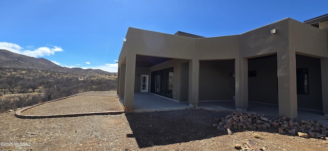 view of side of property with a patio area, a mountain view, and stucco siding