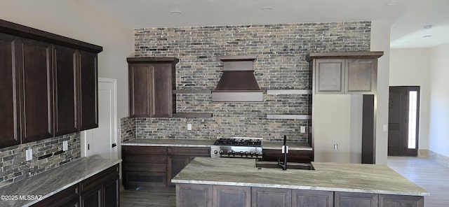 kitchen featuring light stone counters, stove, a sink, dark brown cabinets, and tasteful backsplash