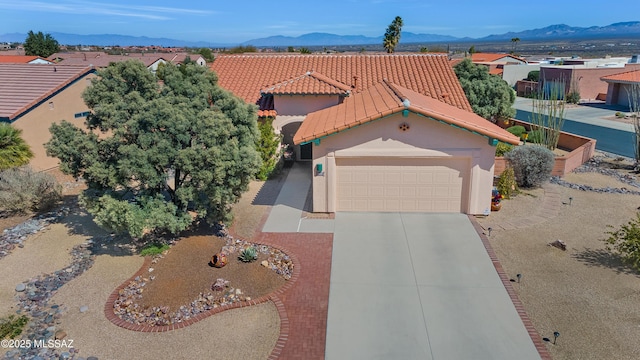 view of front of property with an attached garage, a mountain view, a tiled roof, concrete driveway, and stucco siding