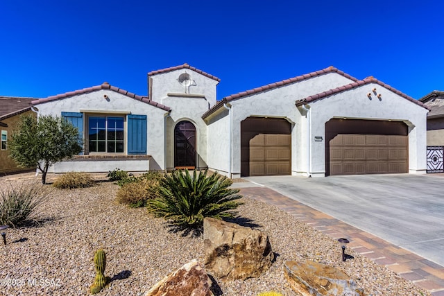 mediterranean / spanish-style house with a tiled roof, a garage, concrete driveway, and stucco siding