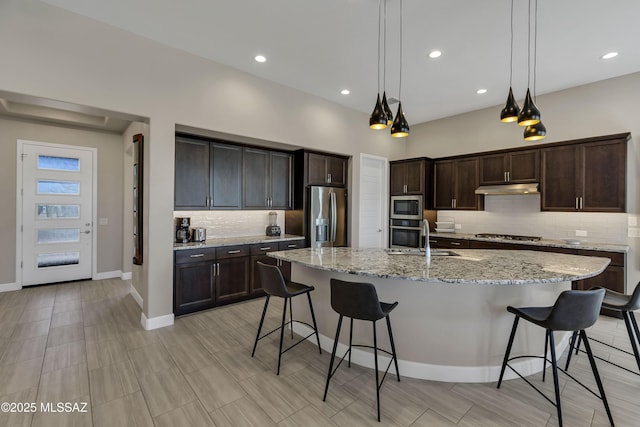 kitchen featuring a sink, dark brown cabinets, under cabinet range hood, appliances with stainless steel finishes, and a kitchen bar