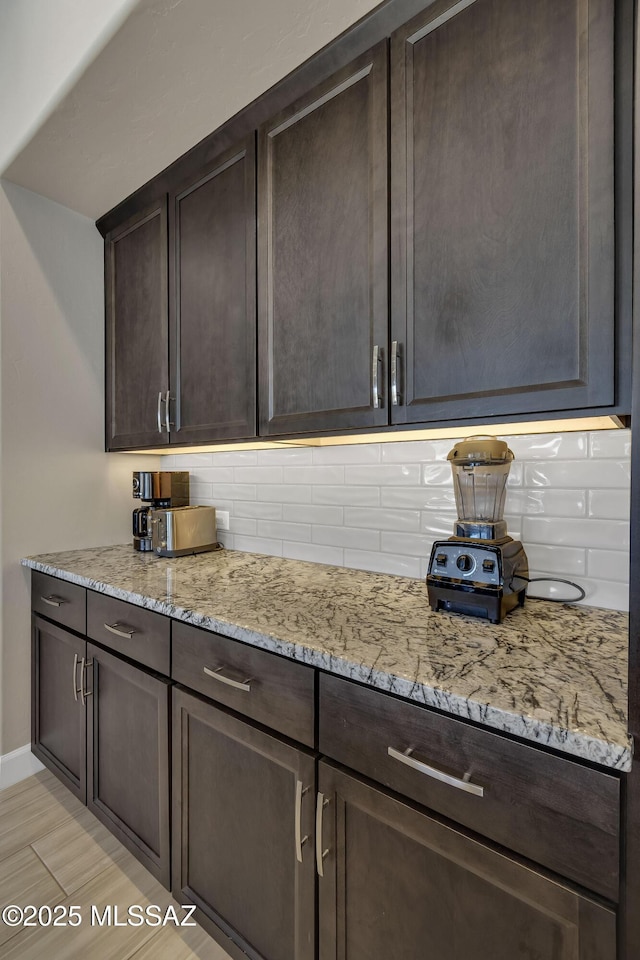 kitchen featuring decorative backsplash, dark brown cabinets, and light stone countertops