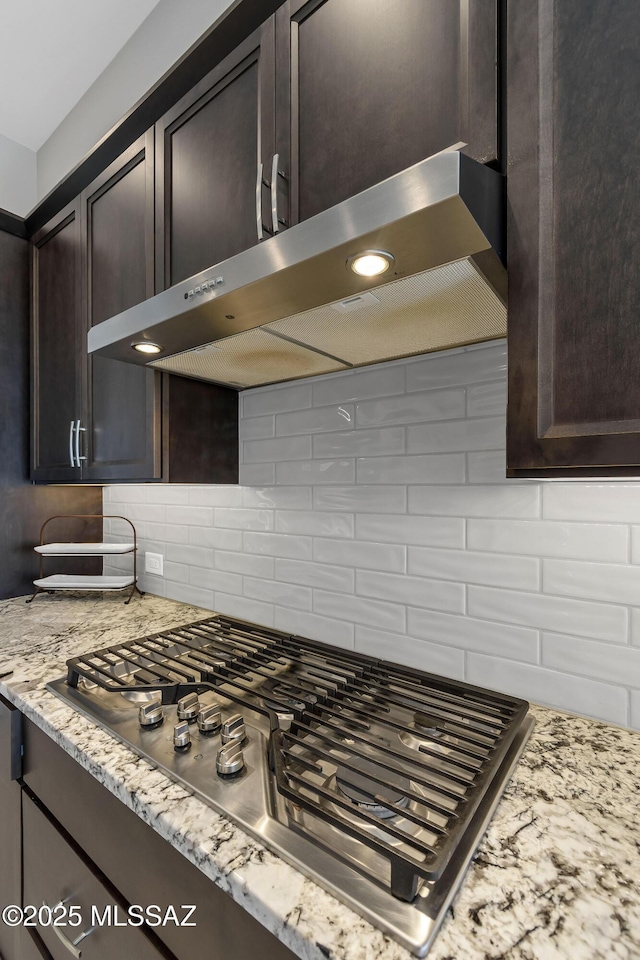 kitchen with tasteful backsplash, stainless steel gas stovetop, dark brown cabinetry, light stone counters, and exhaust hood