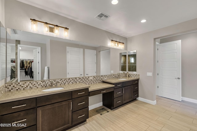 full bath featuring visible vents, a walk in closet, backsplash, baseboards, and vanity