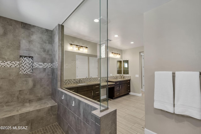 bathroom featuring baseboards, walk in shower, two vanities, recessed lighting, and a sink