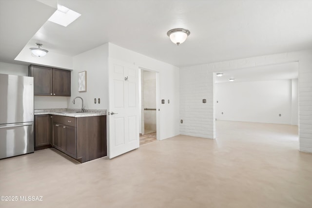 kitchen with dark brown cabinets, finished concrete floors, a skylight, freestanding refrigerator, and a sink