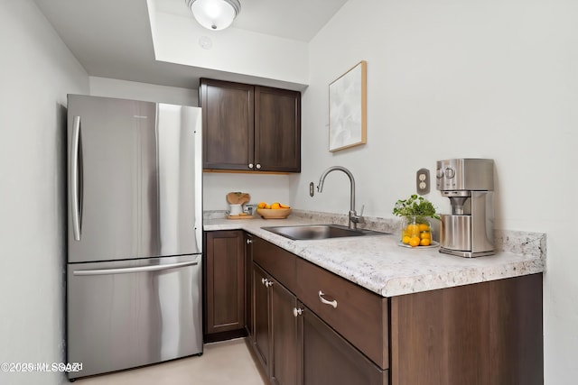 kitchen with a sink, dark brown cabinetry, light countertops, and freestanding refrigerator