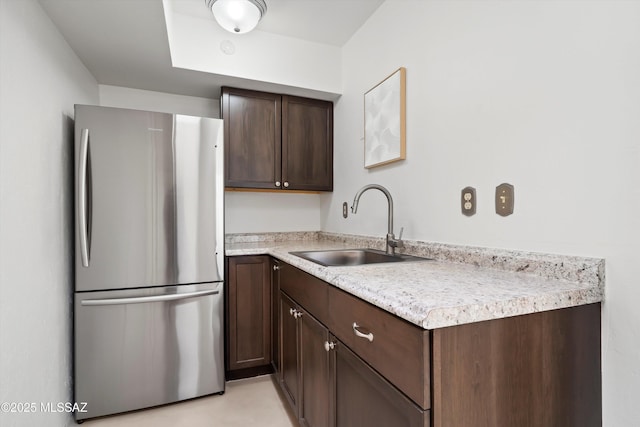 kitchen featuring a sink, dark brown cabinets, light countertops, and freestanding refrigerator