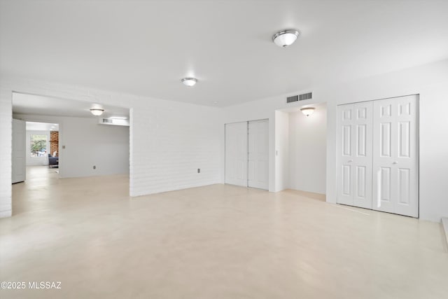 unfurnished room featuring visible vents, brick wall, and finished concrete flooring