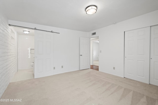 unfurnished bedroom with visible vents, brick wall, a barn door, carpet flooring, and a closet