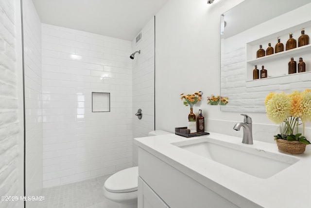 full bath with visible vents, toilet, vanity, and a tile shower