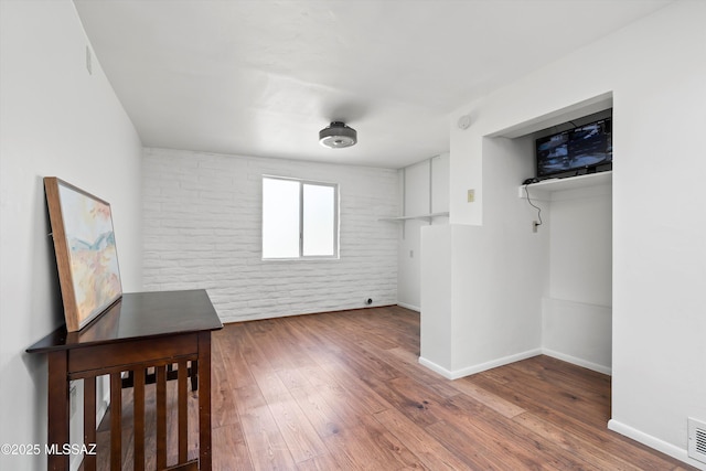 unfurnished bedroom featuring visible vents, baseboards, brick wall, and hardwood / wood-style flooring