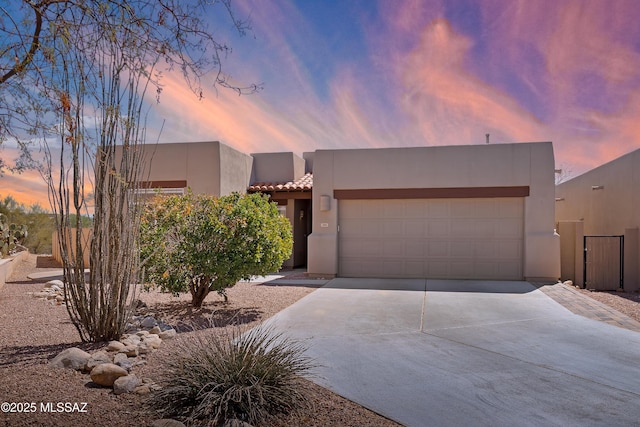 pueblo-style home featuring stucco siding, a garage, concrete driveway, and a tiled roof