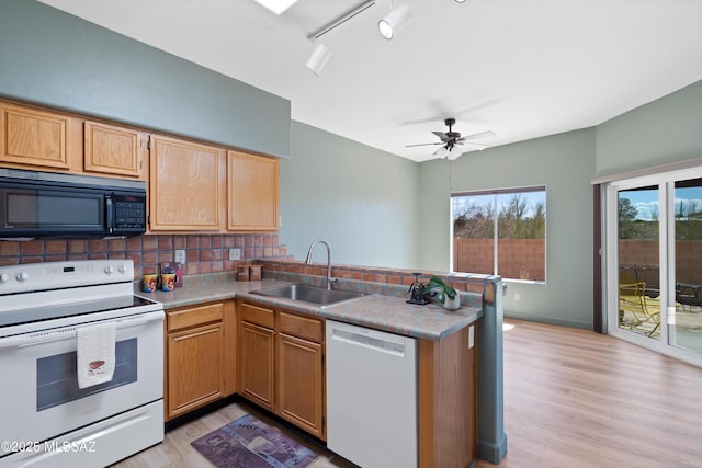 kitchen featuring a sink, light wood-type flooring, white appliances, and a peninsula