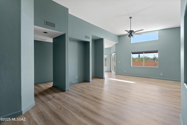 unfurnished living room with visible vents, light wood-style floors, ceiling fan, and a towering ceiling