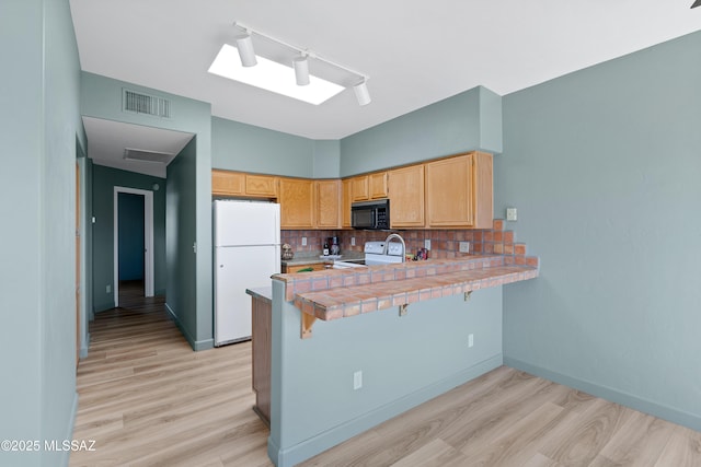 kitchen with light wood-type flooring, visible vents, white appliances, a peninsula, and decorative backsplash