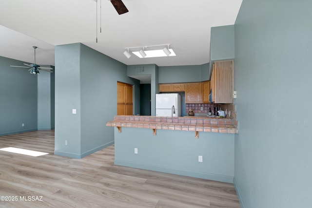 kitchen featuring tasteful backsplash, ceiling fan, tile countertops, a peninsula, and freestanding refrigerator