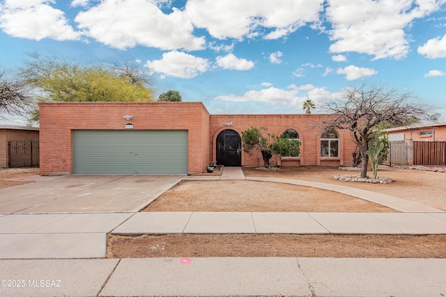 view of front of home with an attached garage, fence, brick siding, and driveway