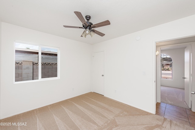 unfurnished room with light tile patterned floors, light colored carpet, and a ceiling fan