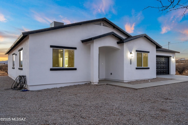 view of front facade featuring stucco siding, central air condition unit, concrete driveway, and an attached garage