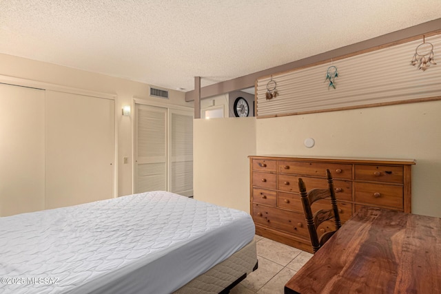 bedroom featuring multiple closets, visible vents, a textured ceiling, and tile patterned floors